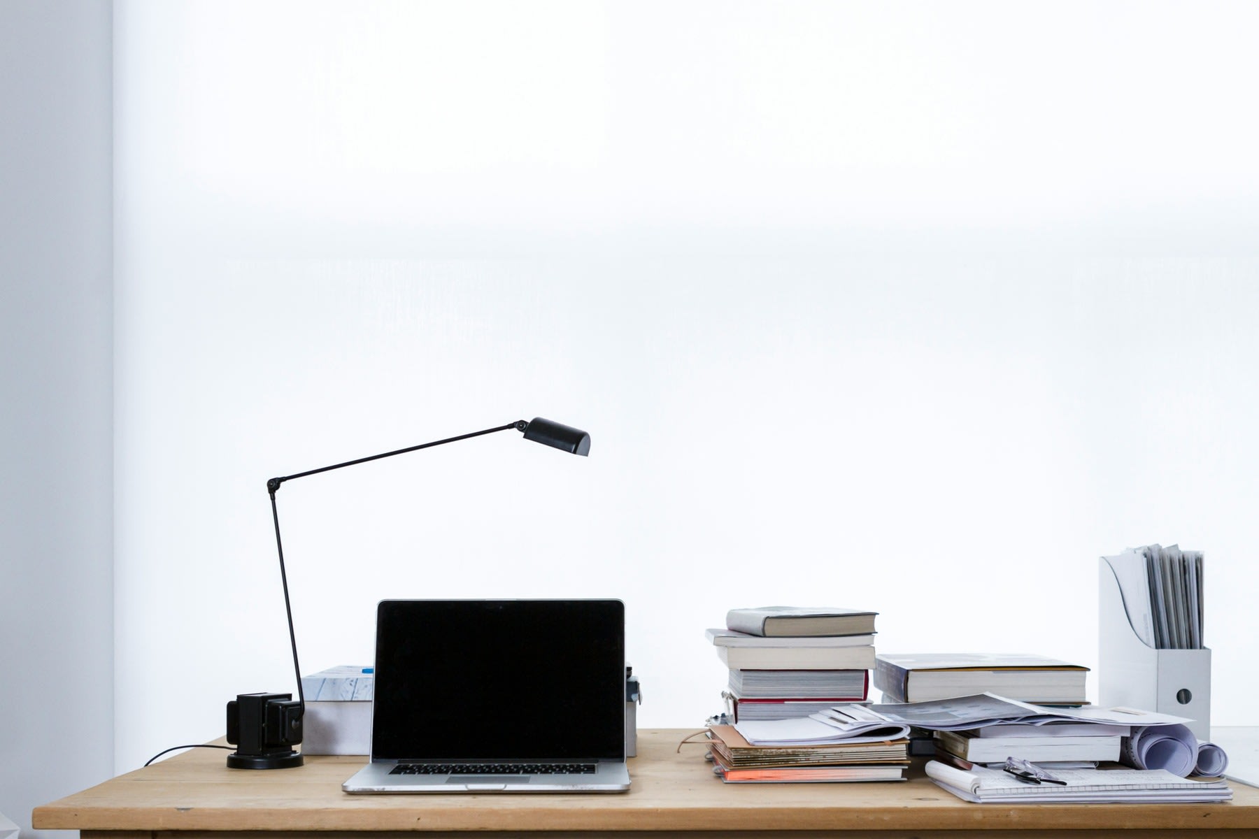 Table with laptop, lamp, stack of books and printed reports
